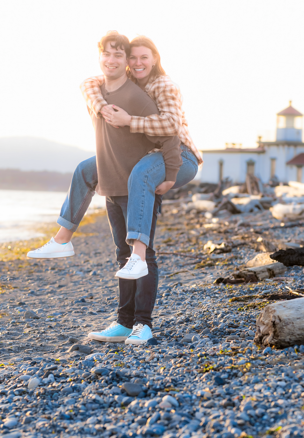 A romantic sunset moment at Discovery Park lighthouse in Seattle with the sun creating a warm backlit glow on the rocky beach.