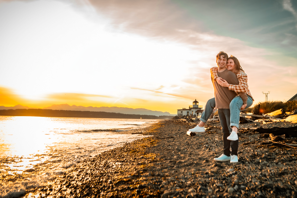 Couple embracing and enjoying a romantic sunset moment on rocky beach with golden light reflecting off the water.