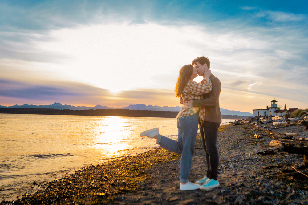 A couple embraces on a rocky beach shore during a golden sunset over calm waters.