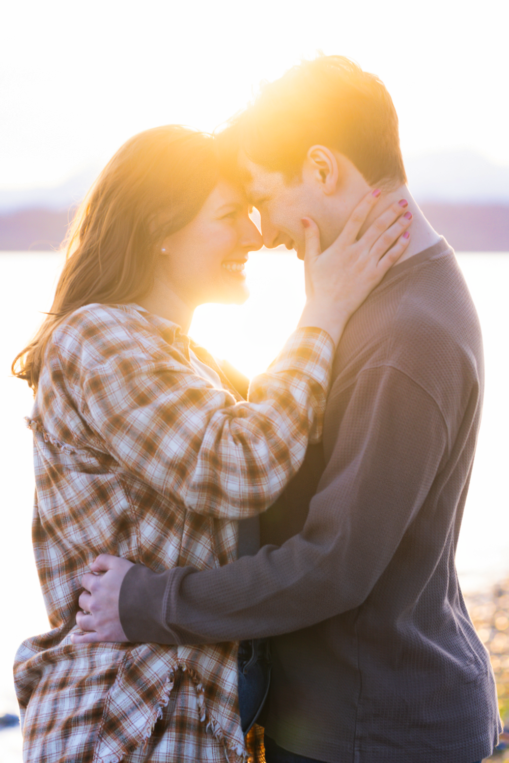 Romantic couple embraces in warm sunset light with woman wearing plaid shirt and man in dark sweater.