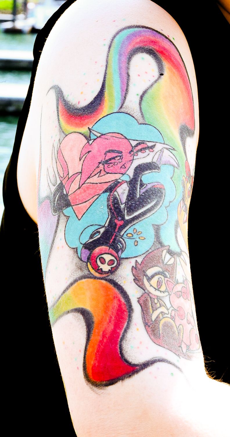 Rainbow-hued arm tattoo showcasing floral elements and animated characters in bright turquoise, pink, and orange tones.