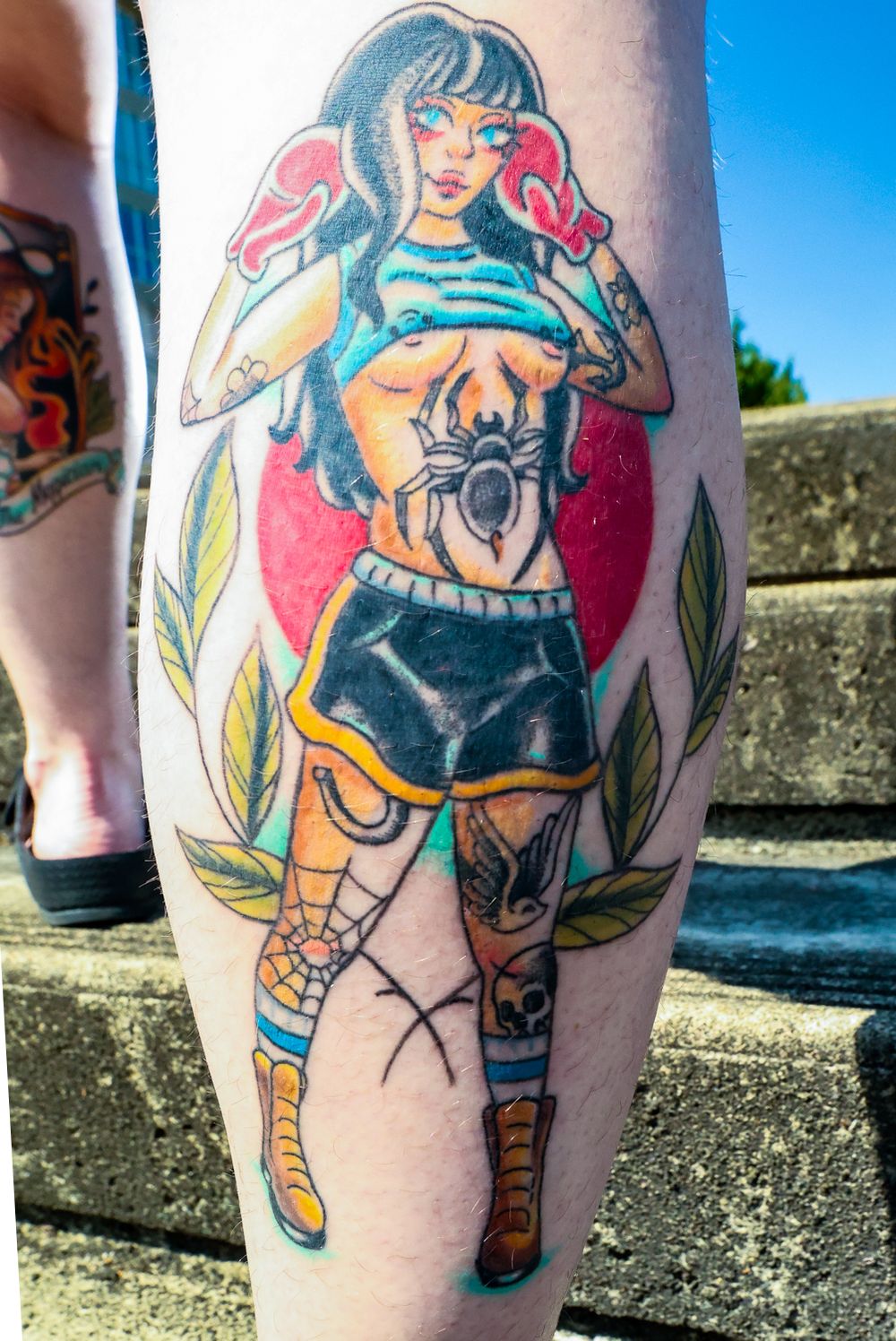 Colorful anime style tattoo showing a figure in blue crop top and black shorts with a spider design surrounded by green foliage.