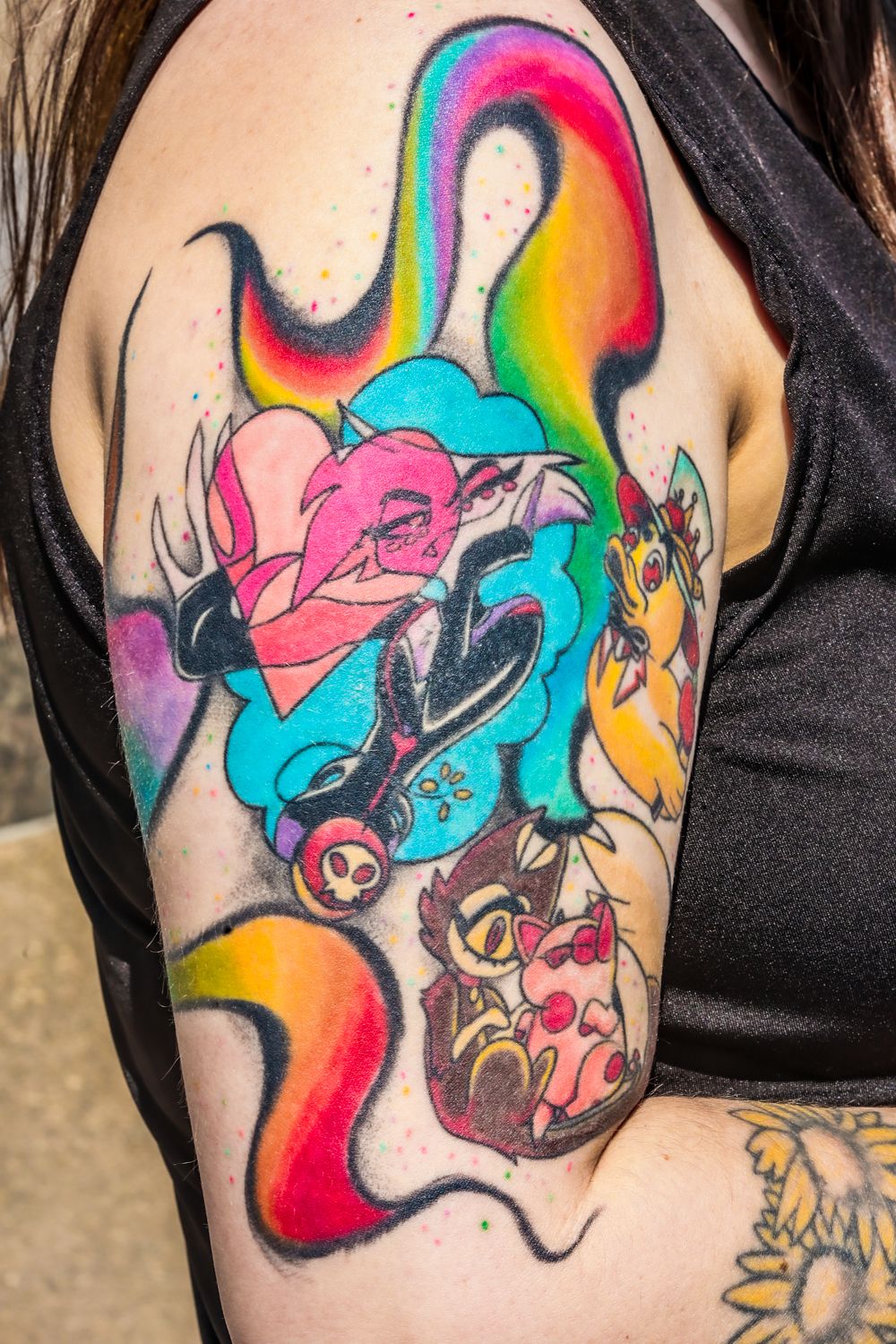 Vibrant arm tattoo featuring colorful rainbow swirls, pink flowers, and cartoon animal characters in a whimsical design.