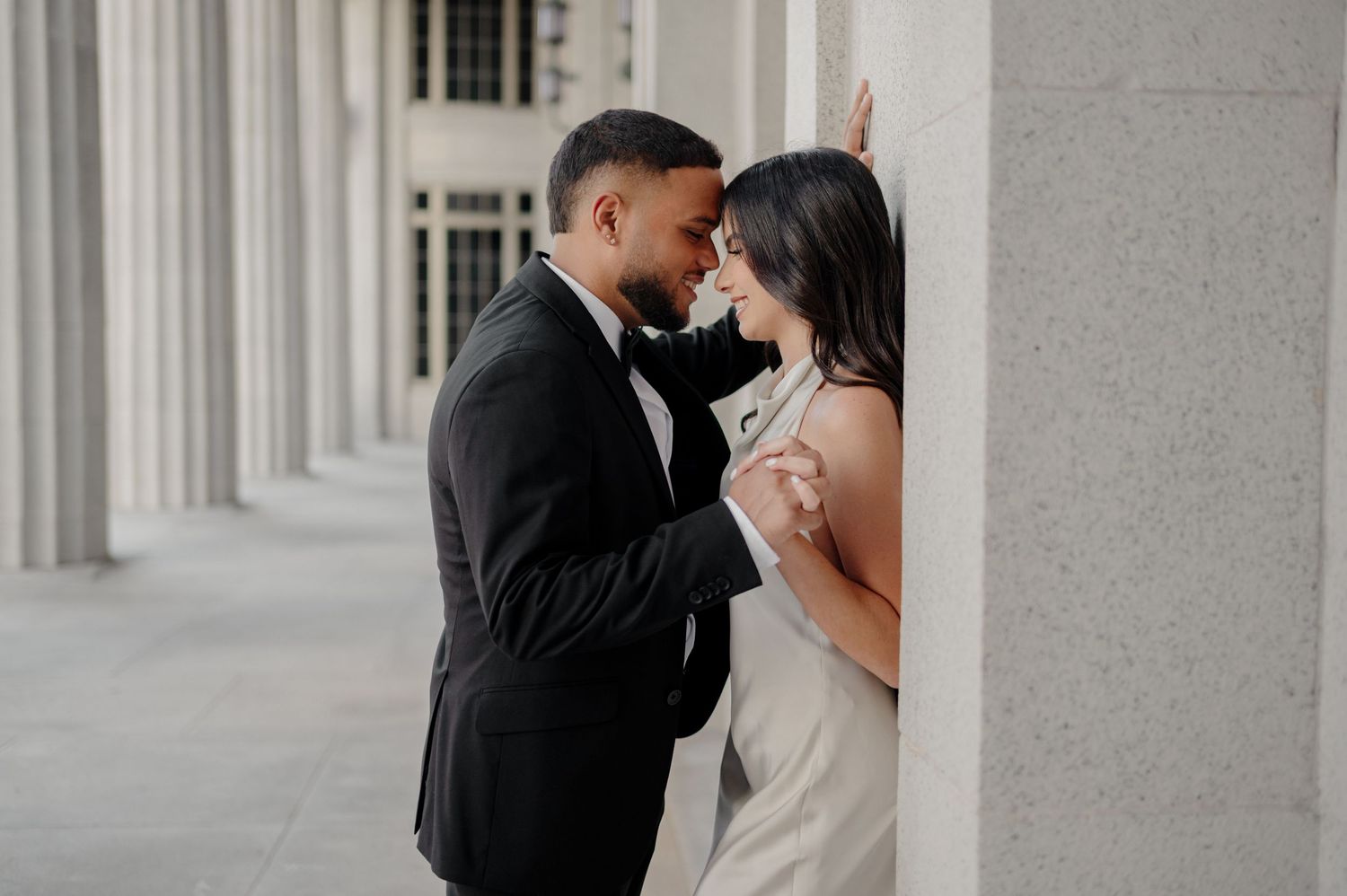 Romantic couple shares an intimate moment in formal attire against classic white columns.