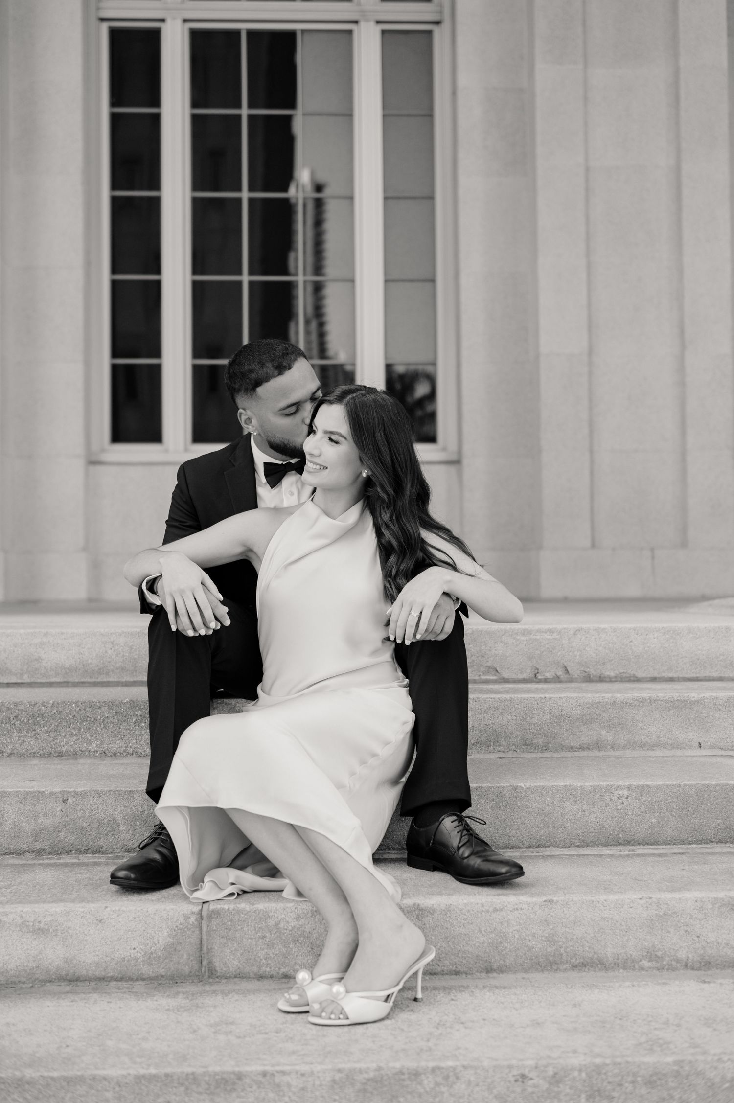 Elegantly dressed couple poses on stone steps in black and white photography.