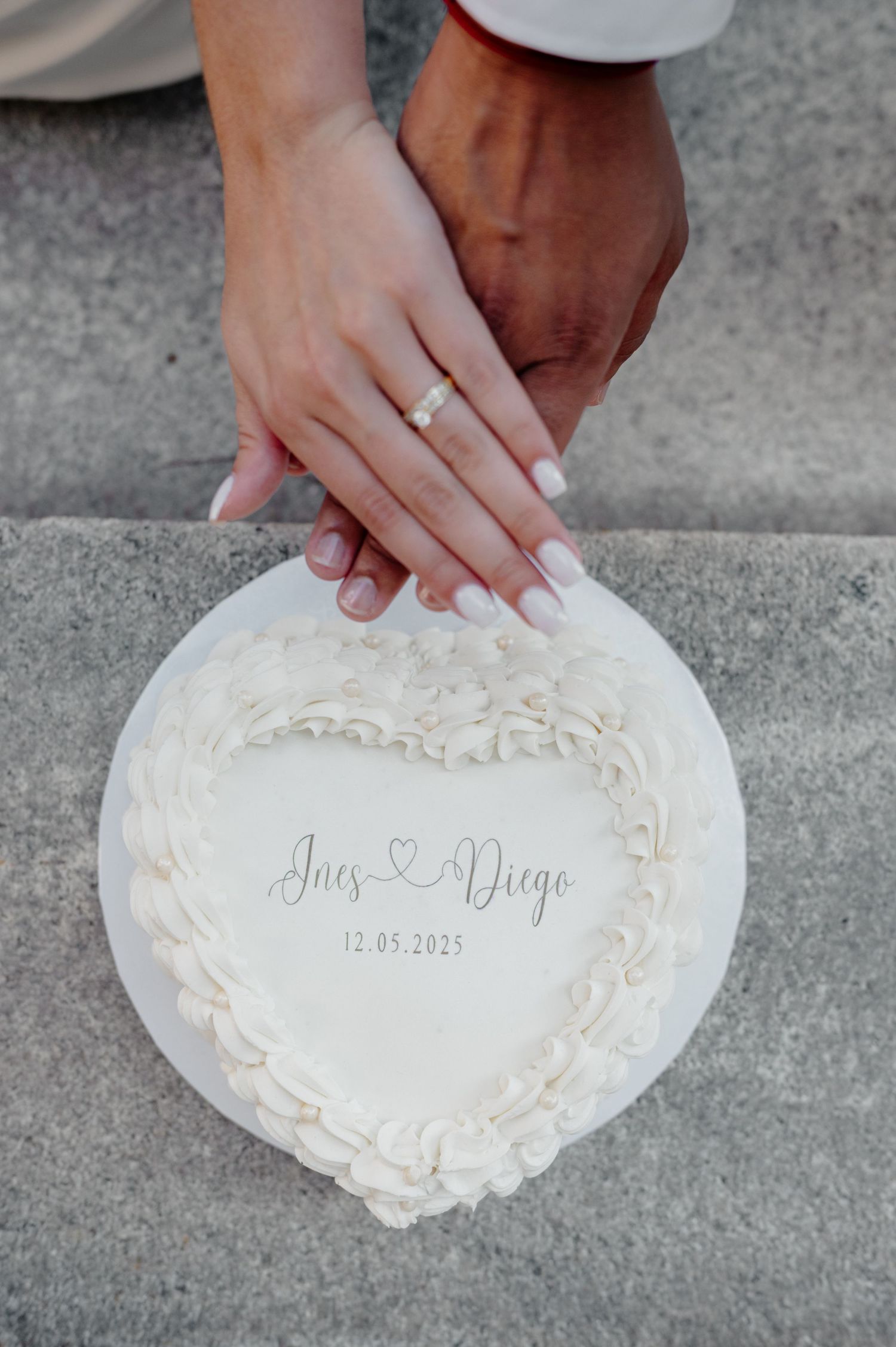Hands displaying engagement ring rest on white heart-shaped plaque with names and wedding date engraved.