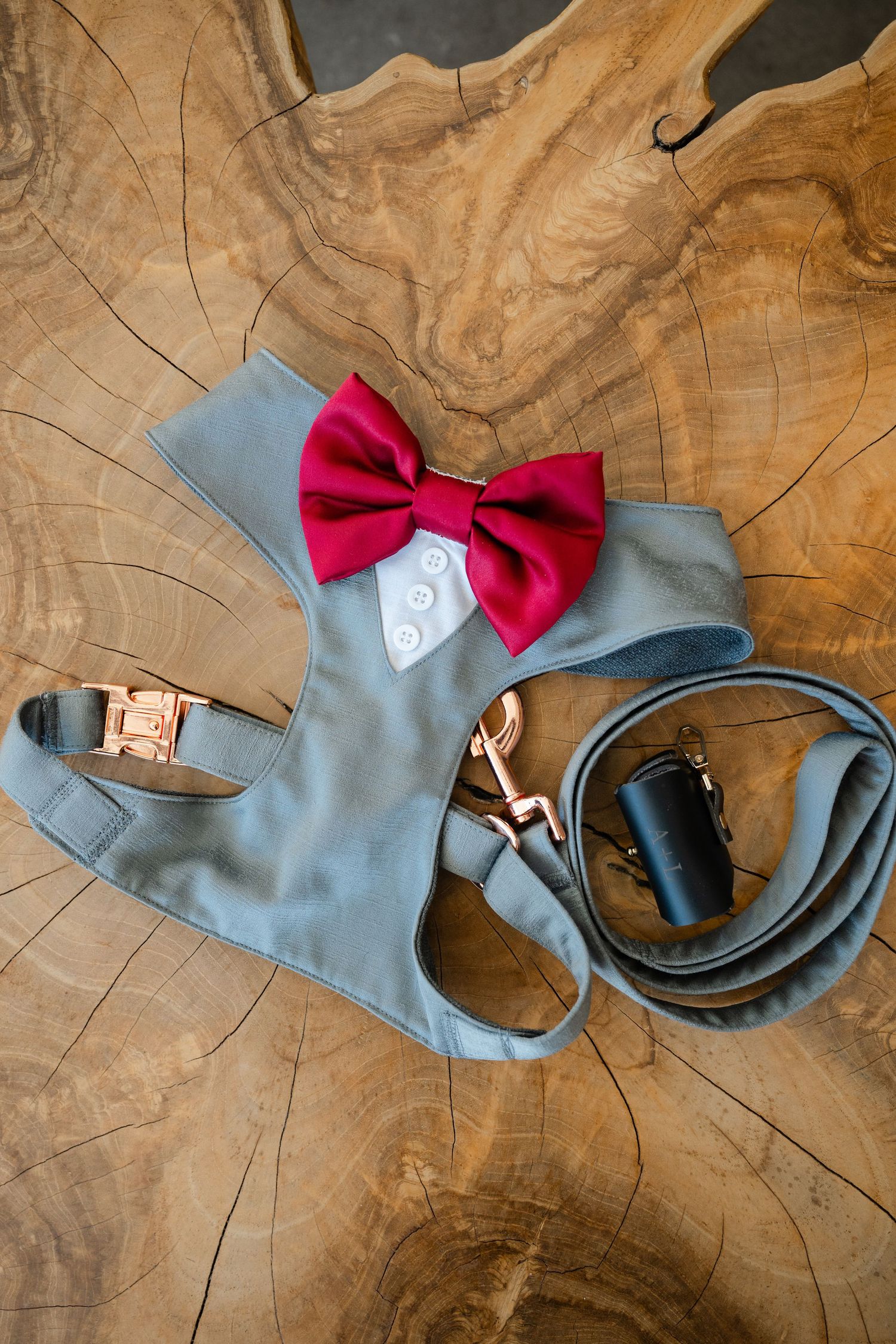 Black leather dress shoes with belt and engagement ring box arranged on wooden surface.