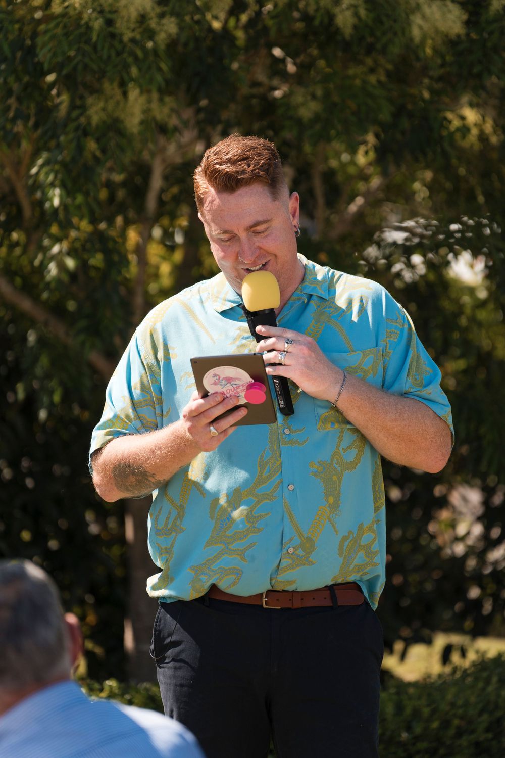 A speaker at an outdoor event holds a microphone and refers to notes during a presentation.