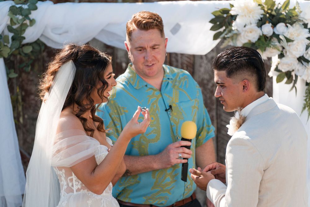 A wedding ceremony takes place under a floral arch with a group conversing during the celebration.