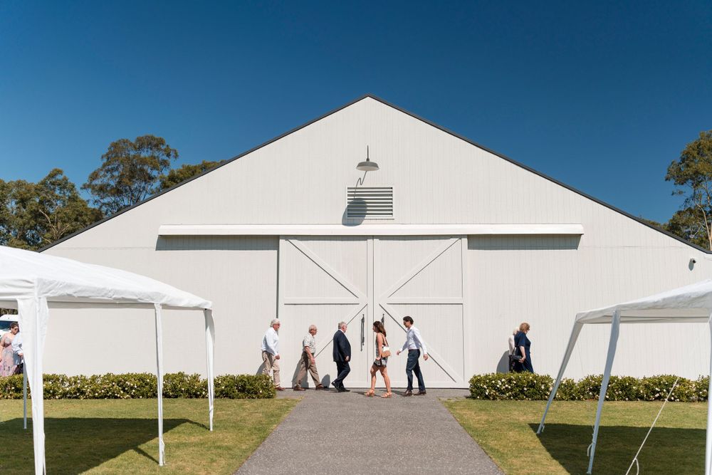 A white barn-style event venue with sliding doors and outdoor tent canopies against a bright blue sky.