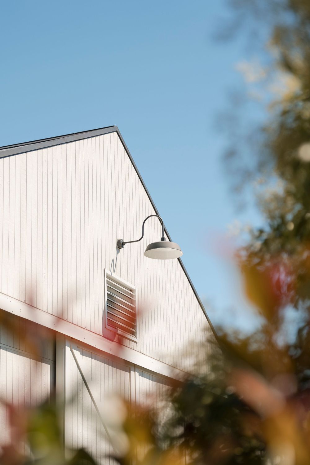 Close-up view of a white barn exterior with vintage barn light against a bright blue sky.