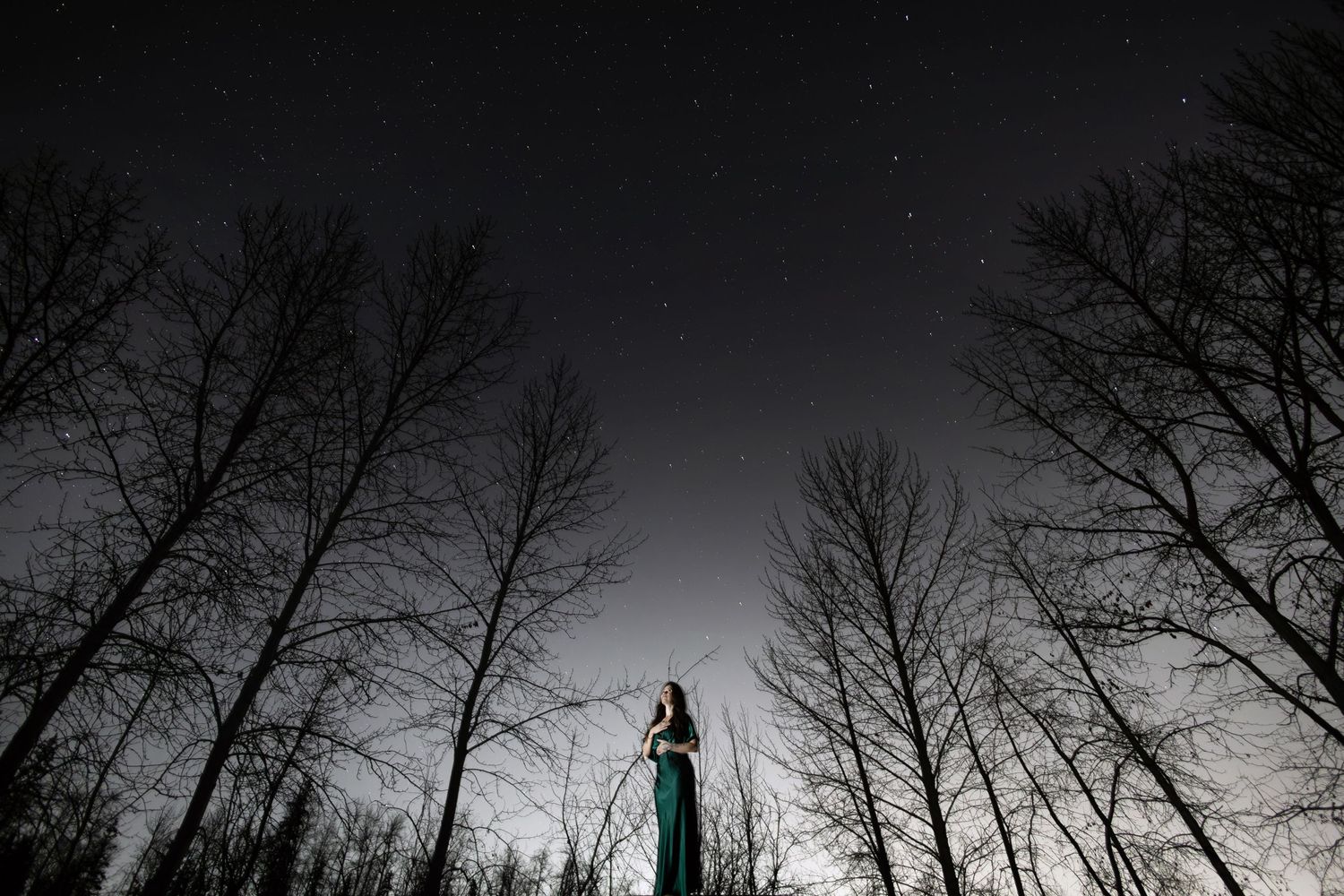Mandy Trapp, meditation leader and breathe worker in a dress stands elevated against a dark night starry sky in Edmonton Alberta