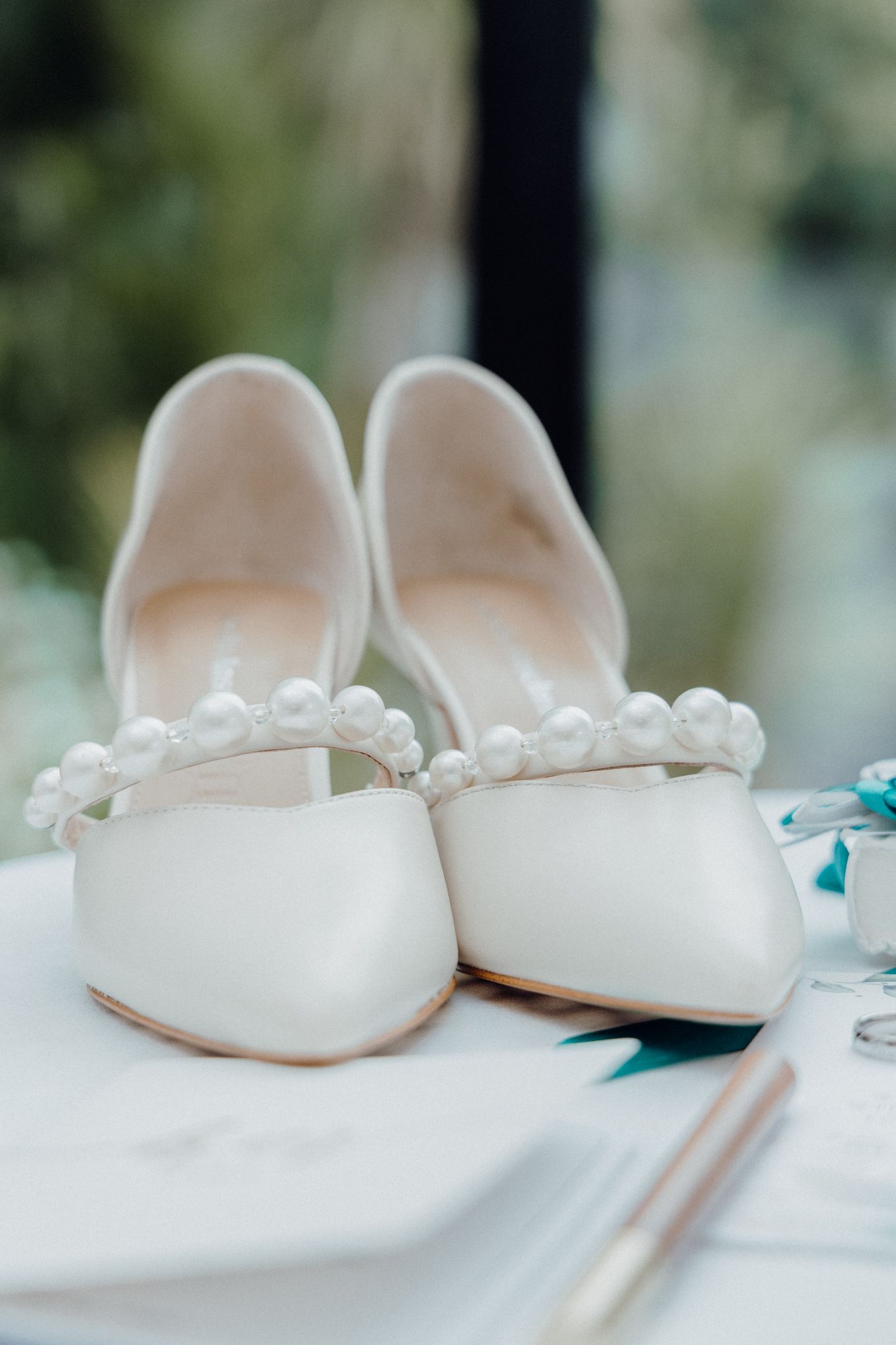 White bridal flats adorned with pearl details rest on a light surface captured by Apertured Media Auckland Wedding Photographer.