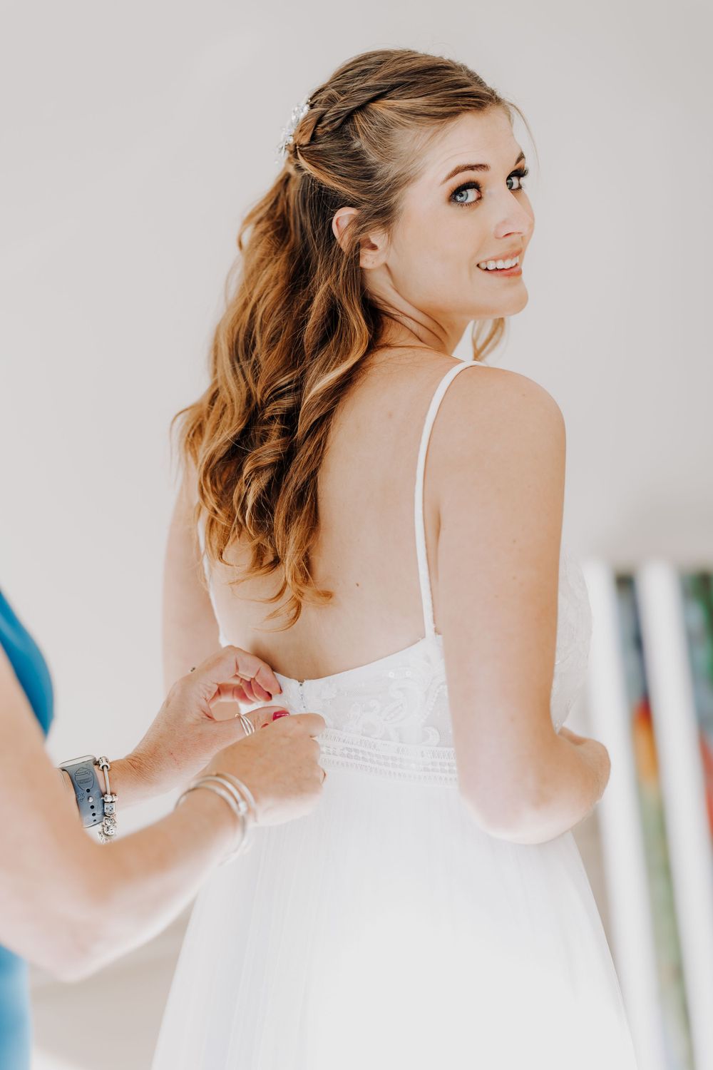 Bride getting their wedding dress adjusted while looking over their shoulder with a smile.
