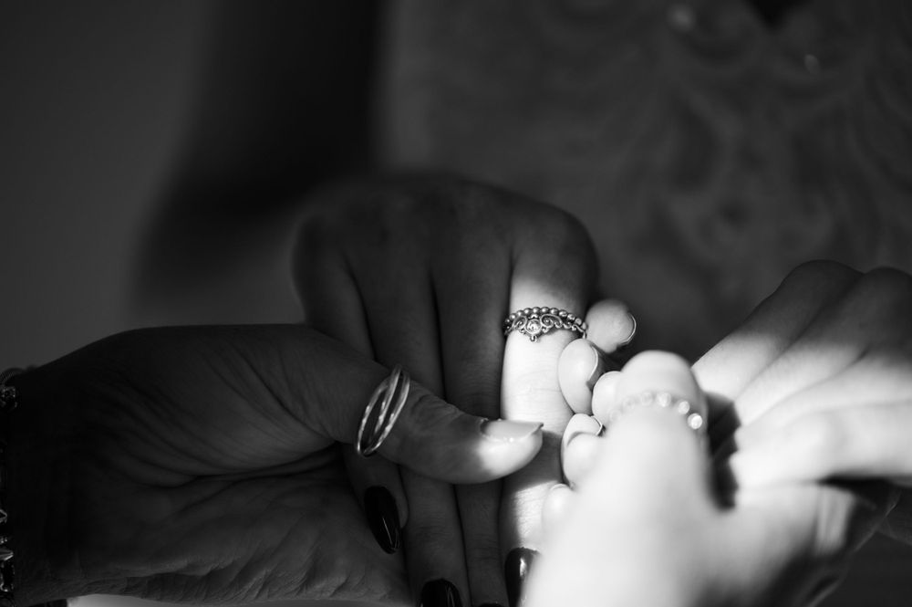 Close-up black and white shot of wedding rings being placed on fingers.