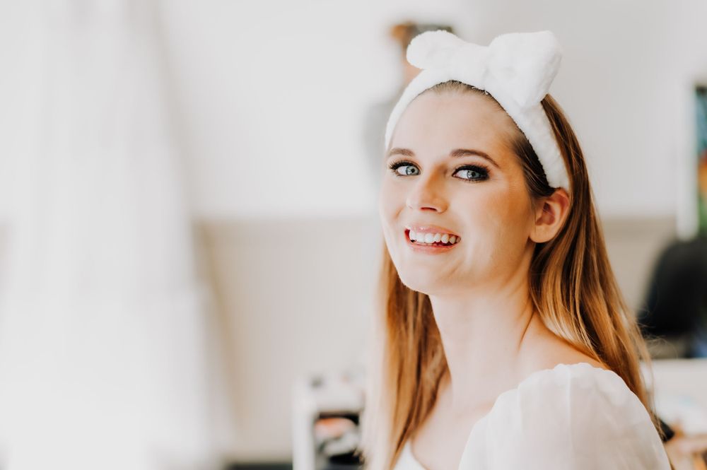 Candid bride preparation photo showing joyful expression in white robe and headband.