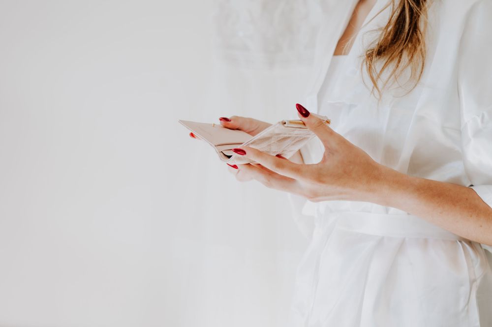Elegant hands with red manicure holding white tissue paper against light background.