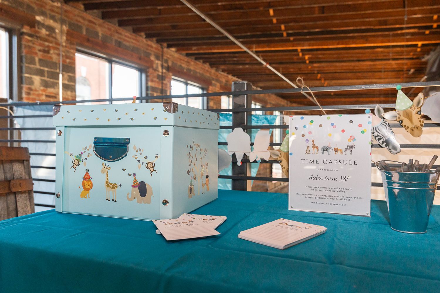 Time capsule display with decorative box on turquoise tablecloth against brick wall.