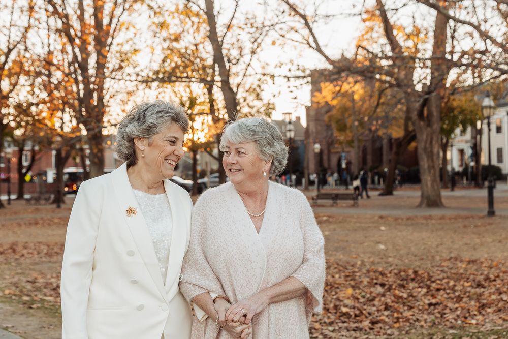 Two people in white outfits walking through an autumn park with fallen leaves.