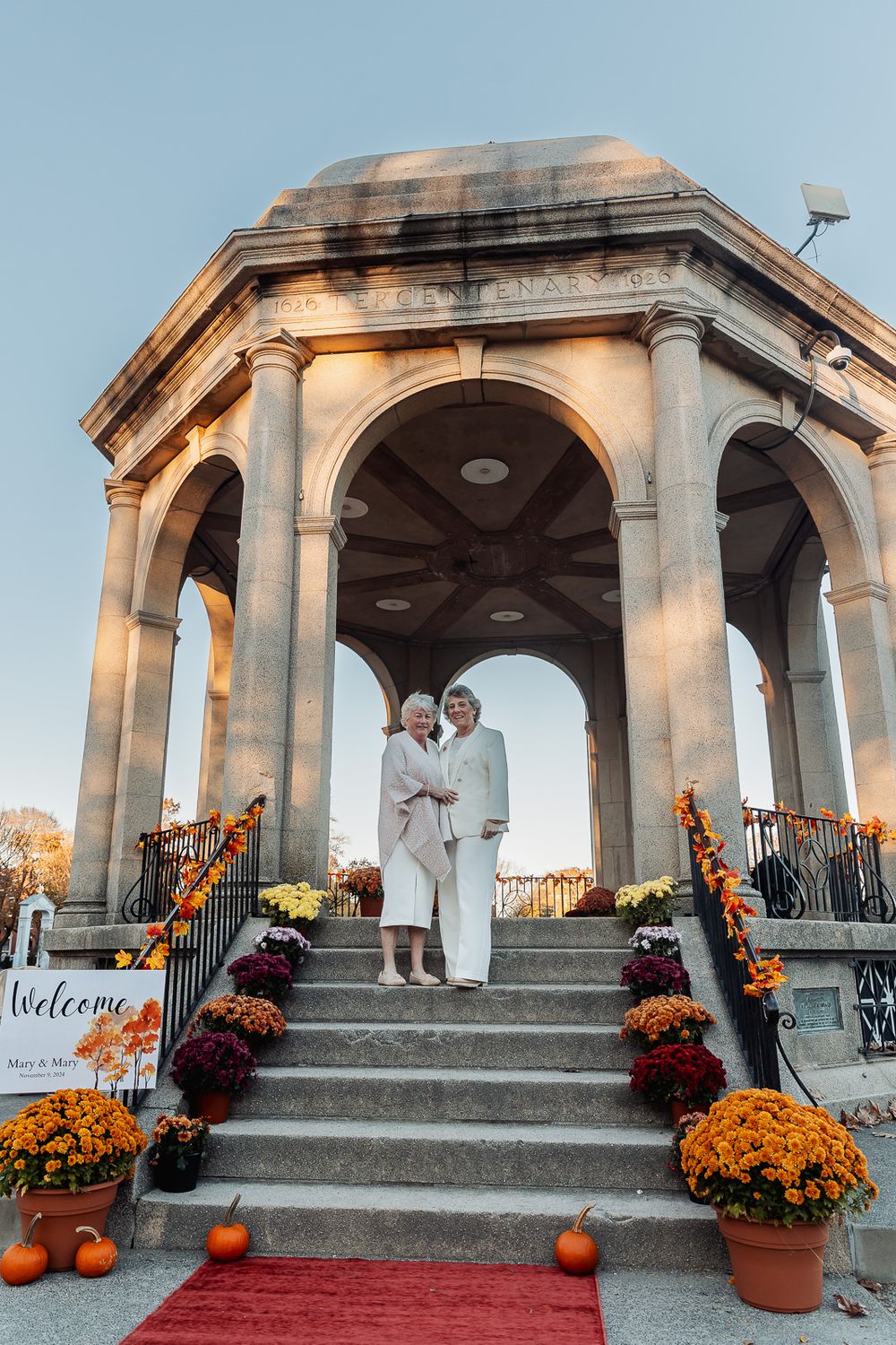 Decorated gazebo with orange mums and pumpkins for autumn wedding ceremony.