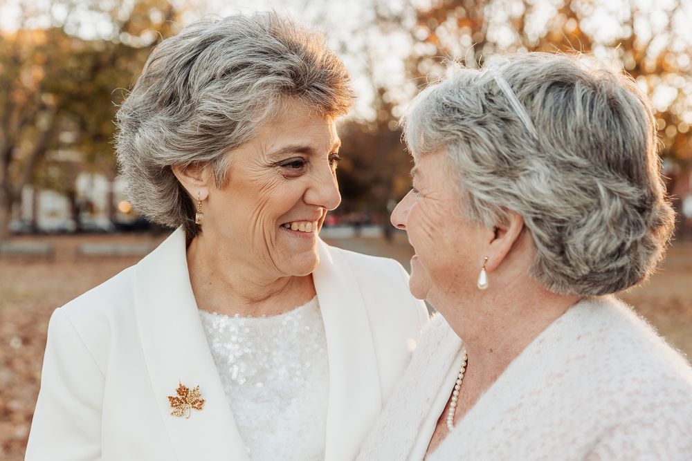 A tender autumn wedding moment captured as a couple in white outfits share a laugh together.