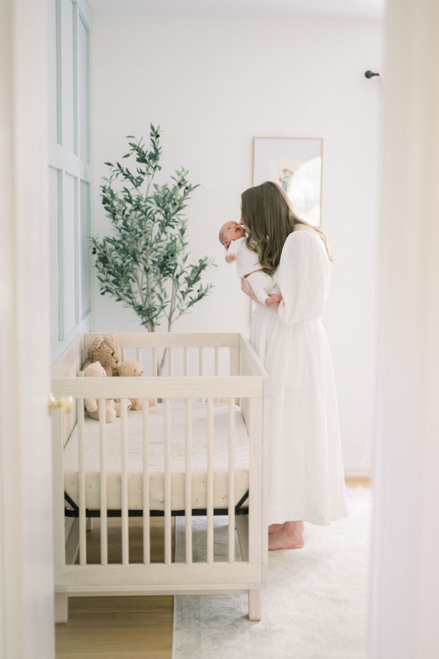 Soft and dreamy nursery scene with white crib and potted plant against light walls creating a peaceful ambiance.