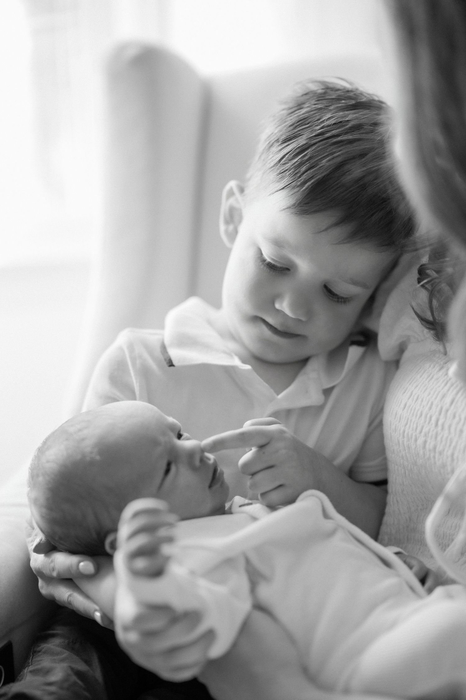 A tender black and white portrait of a young child gently holding and gazing at a newborn baby.