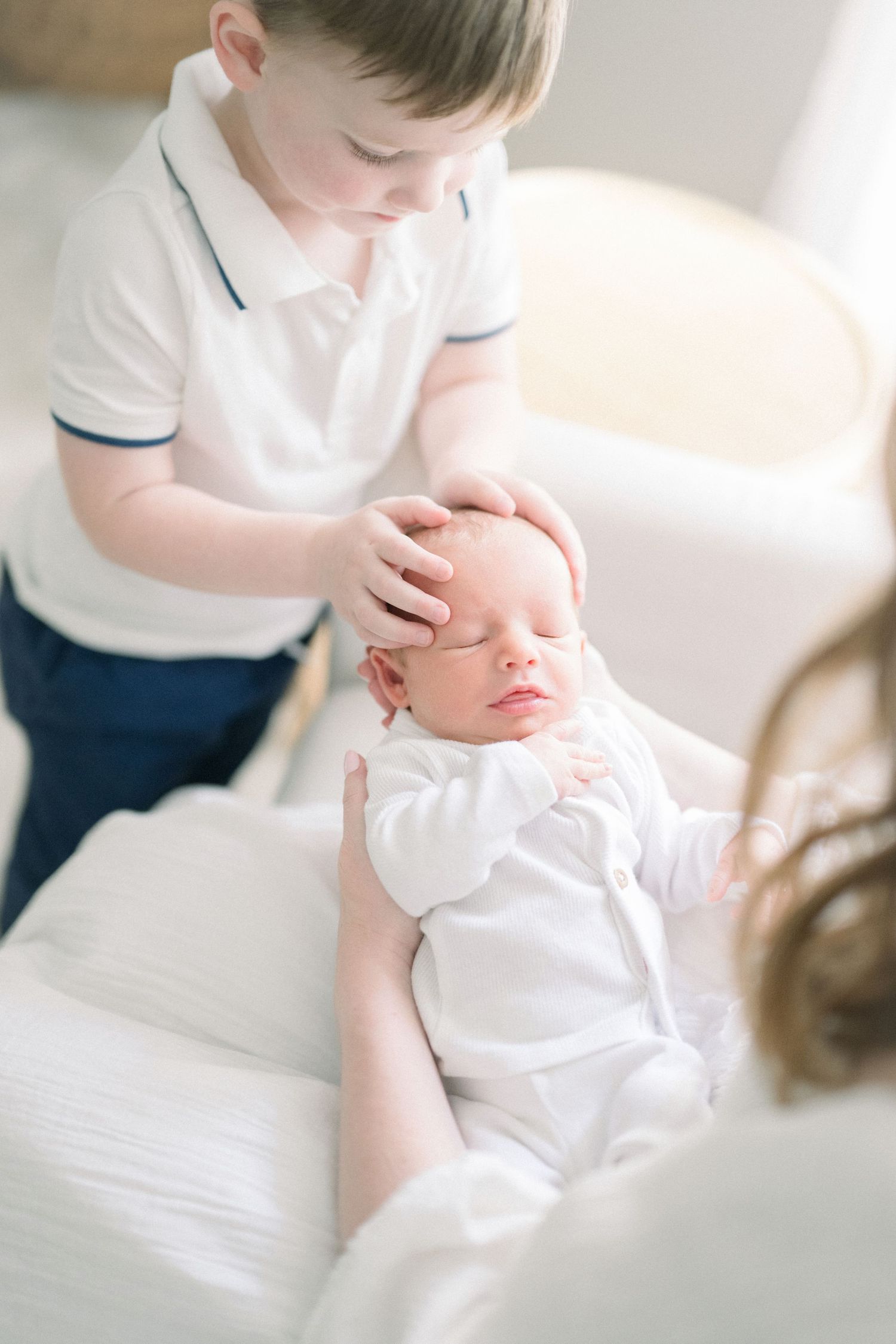 Gentle caring moments captured in white tones showing delicate interactions with an infant.