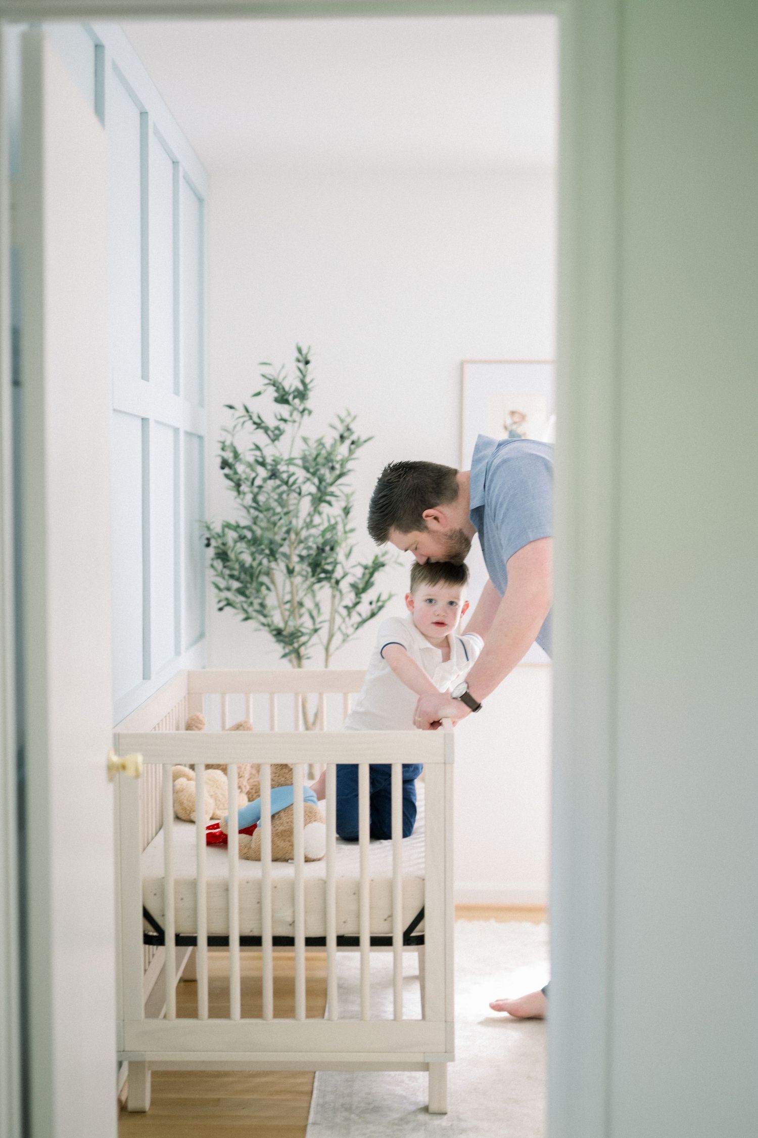 A modern nursery features a wooden crib set against light green walls with natural decor elements.