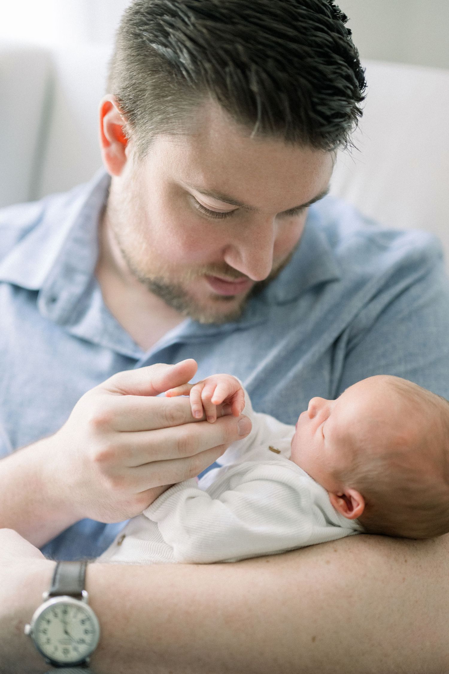 A parent holds and tenderly kisses their newborn baby who is swaddled in a white blanket.