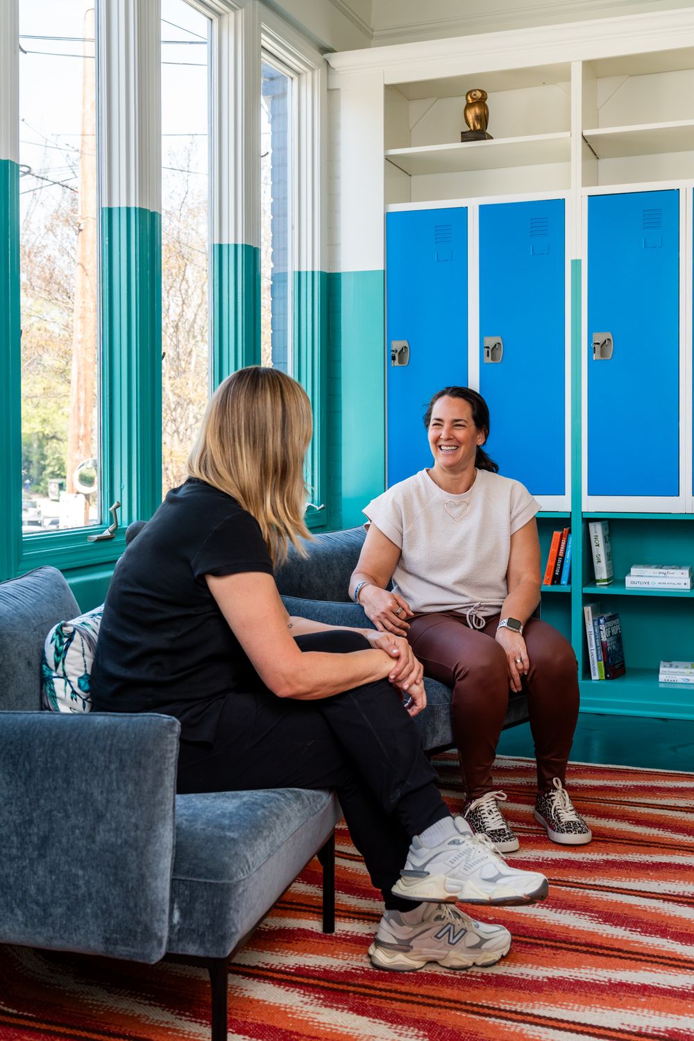 People having a casual conversation while sitting on gray couches in a bright room with blue walls.