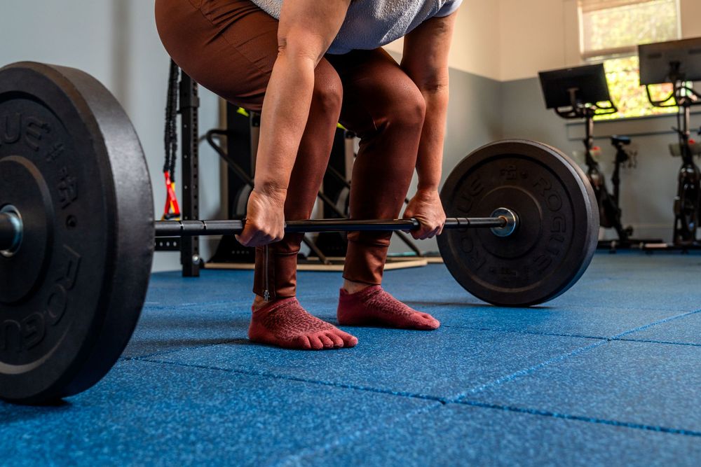 Physical therapist adjusts weight lifting form and technique for patient exercising on blue gym floor.