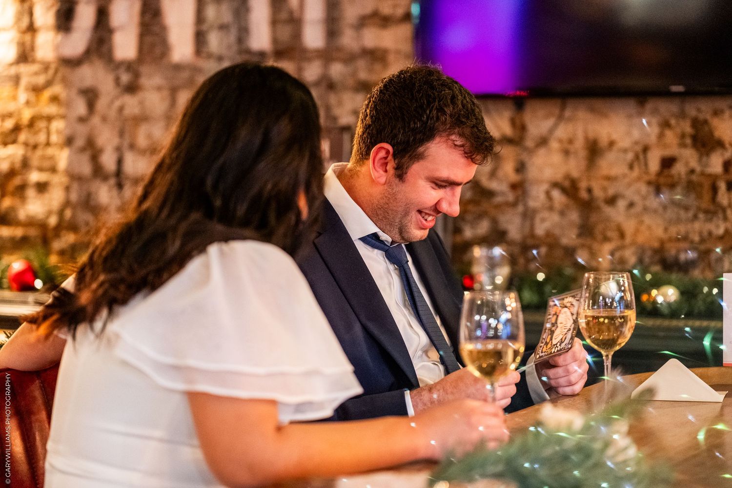 Two dinner guests seated at a restaurant table with wine glasses and warm lighting on stone walls.