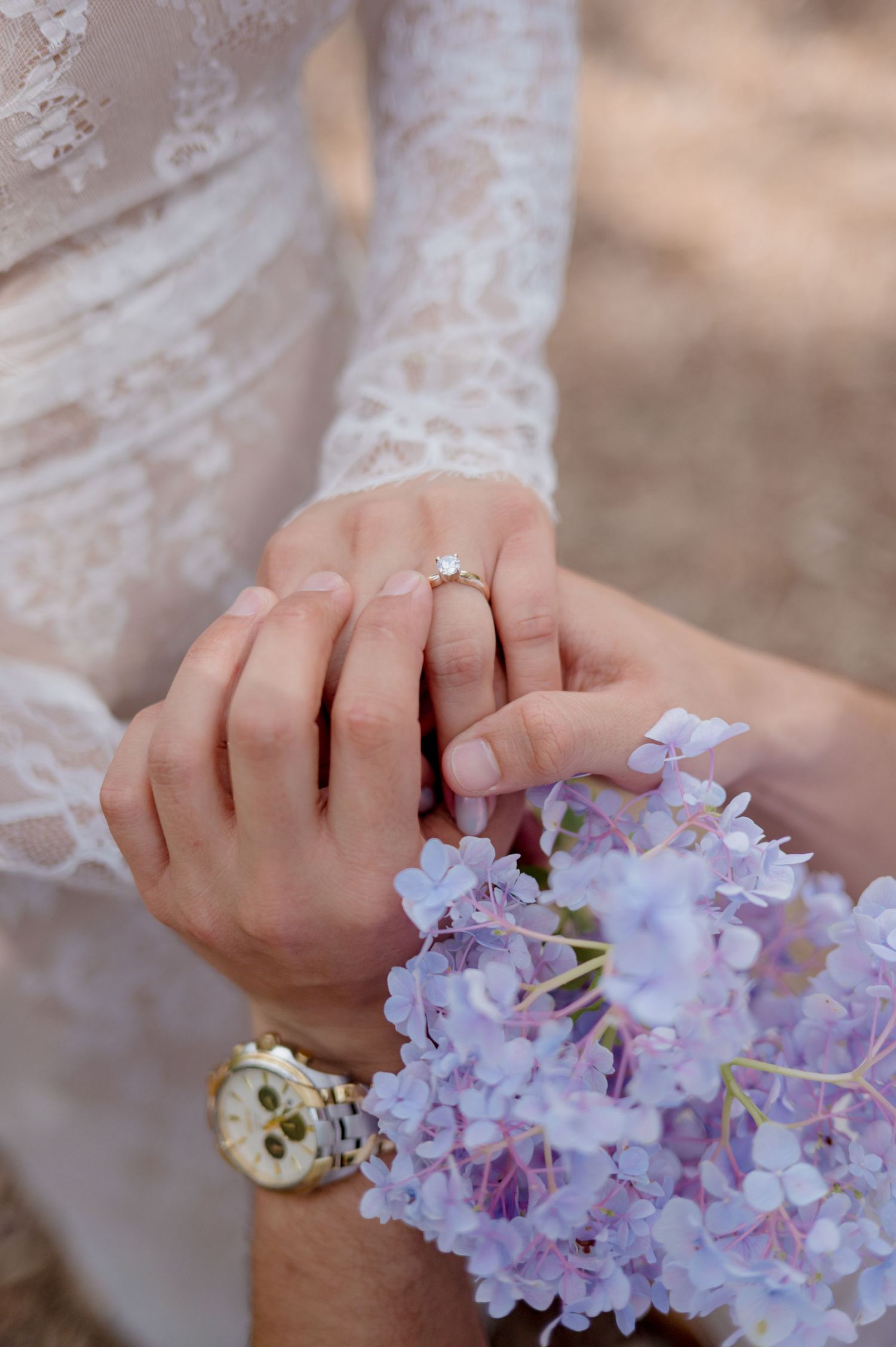 Close-up of hands displaying an engagement ring with delicate purple wisteria flowers and lace sleeve details.