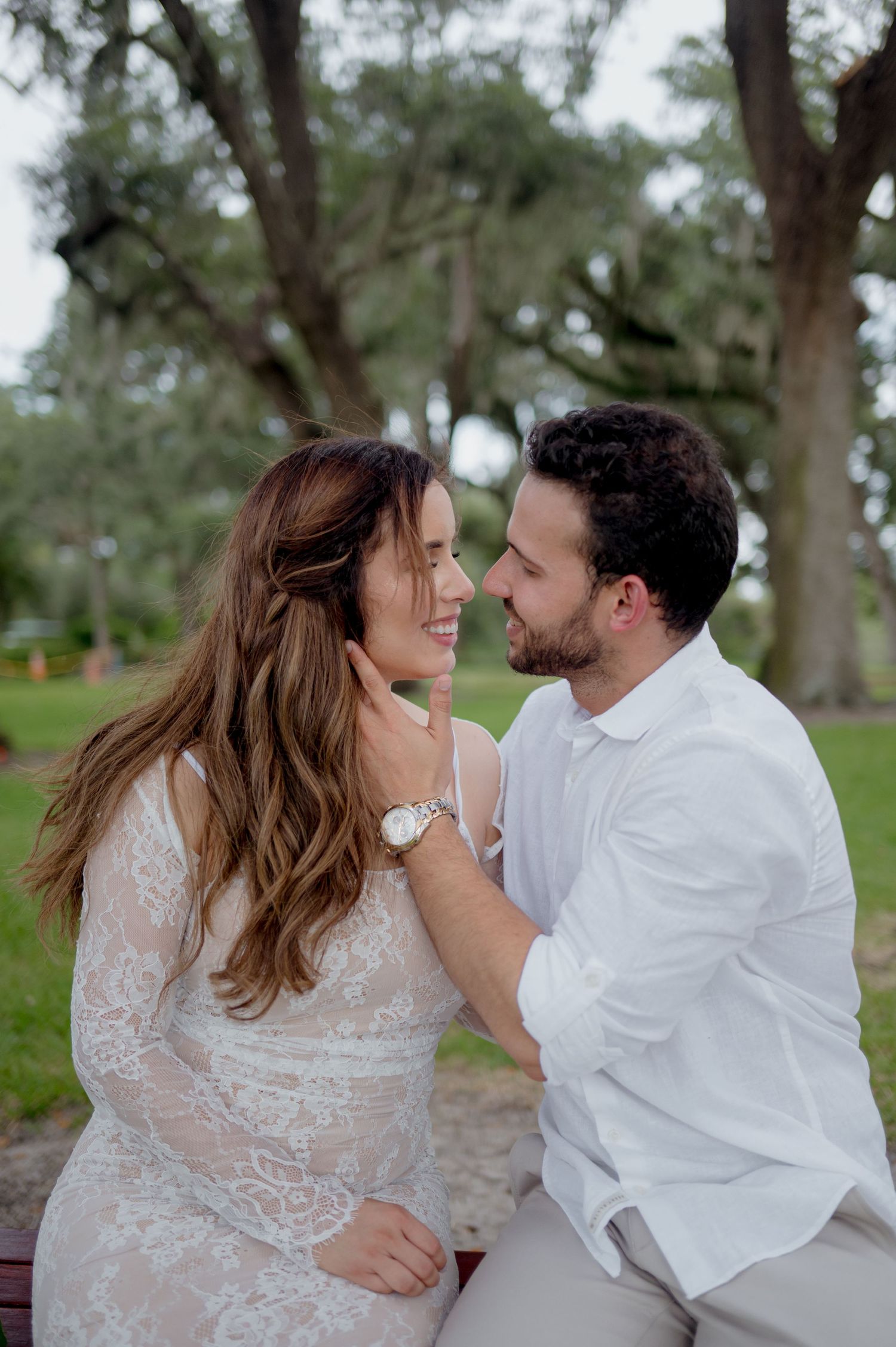 A romantic engagement moment shared between a couple outdoors with trees in the background.