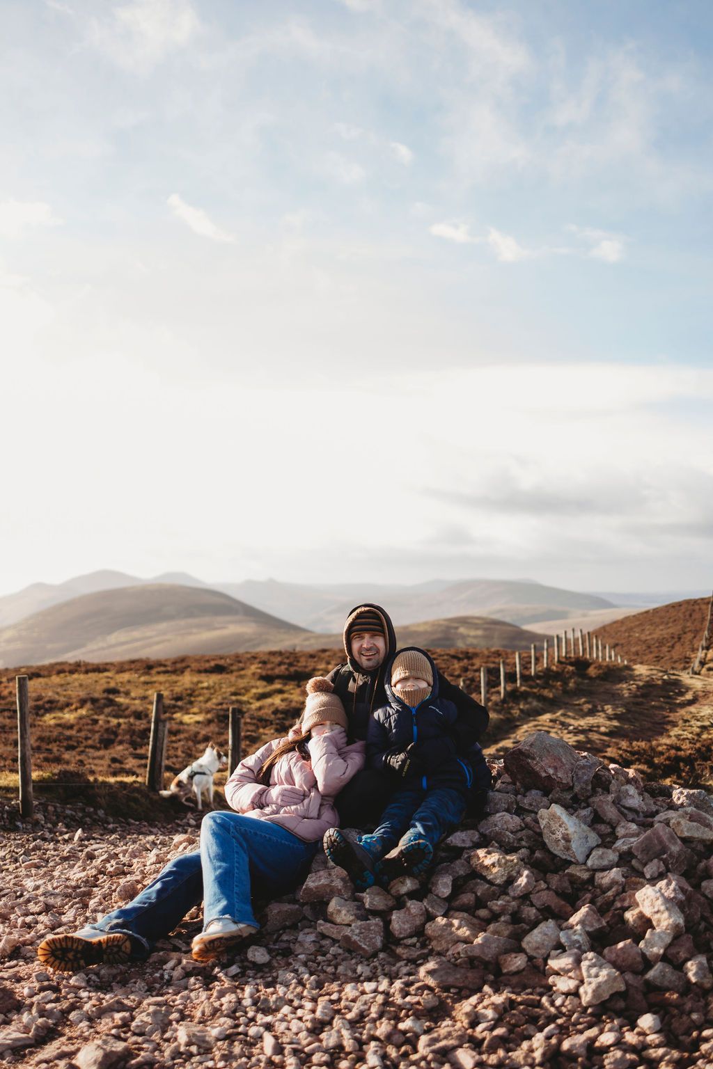 Two people walk through a vast mountain landscape with rolling hills on a cloudy autumn day in Scotland.