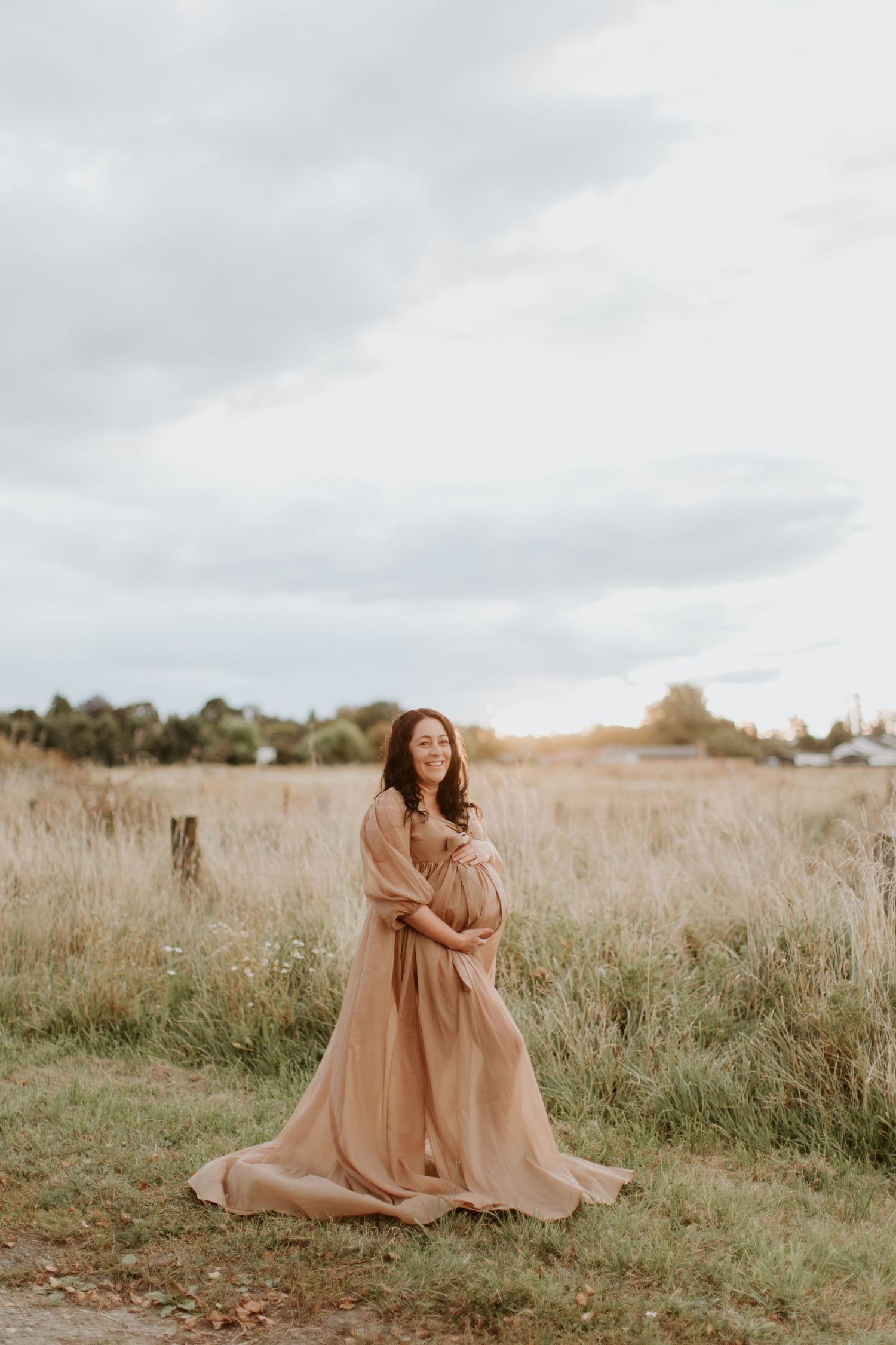 A serene field scene with figures in flowing peach-colored dresses dancing and embracing in tall grass at sunset.