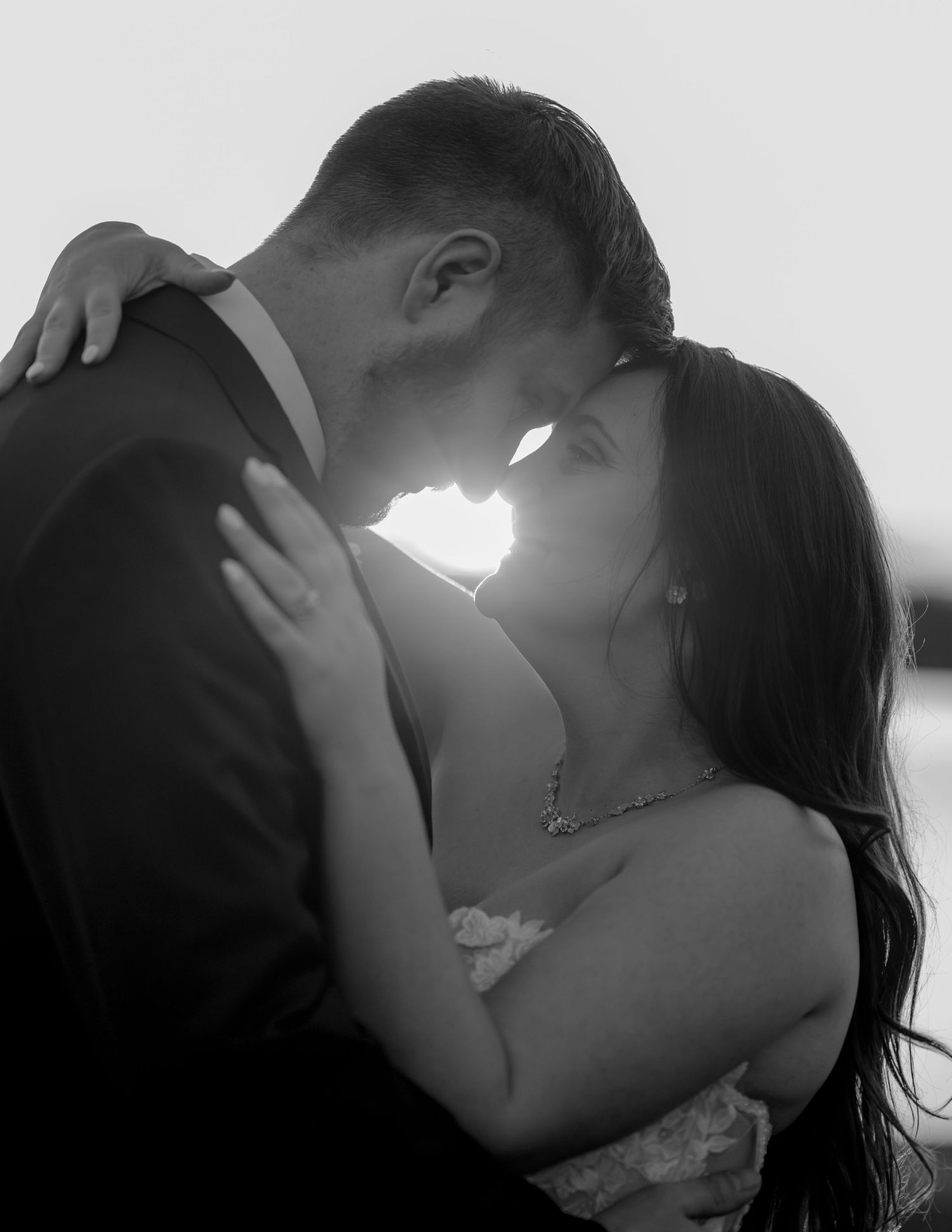 Silhouetted couple sharing a romantic kiss against bright sunlight in a dramatic black and white photo series.