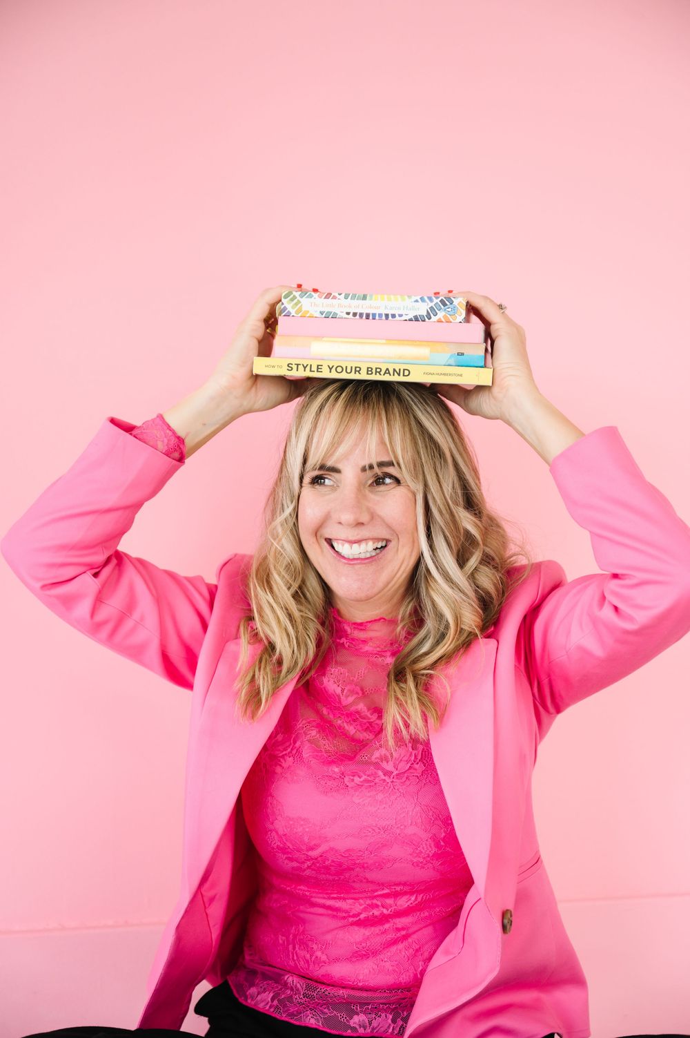 A series of studio portraits with pink background showing someone in a bright pink blazer and lacy top.