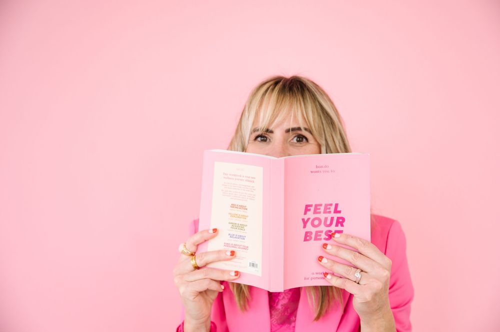 A pink book with white text is held up against a pink background creating a monochromatic aesthetic.