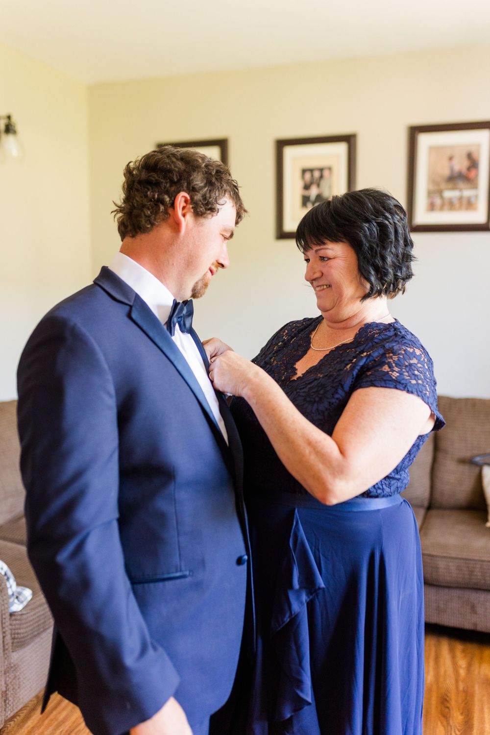 A tender moment of adjusting formal attire during wedding preparations in a living room setting.