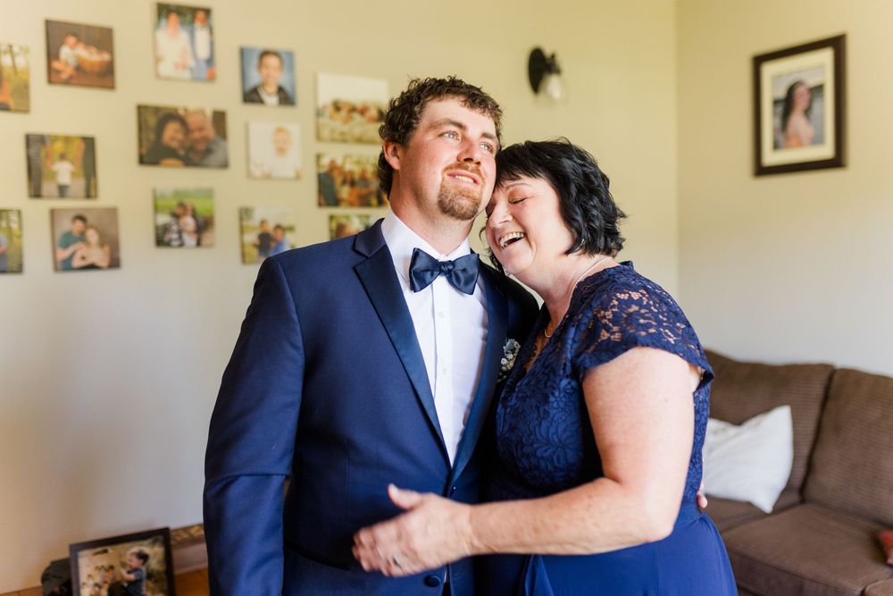 A couple in formal navy and lace attire share an intimate laughing moment against a wall of family photos.
