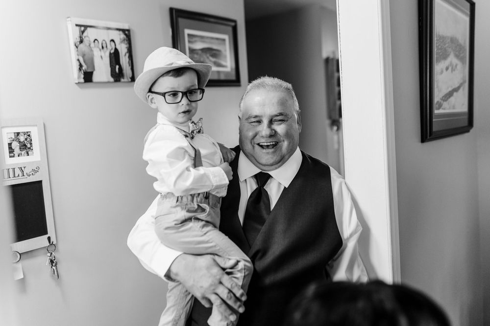 A joyful black and white portrait of a young child in glasses being held by a smiling elder in formal attire.