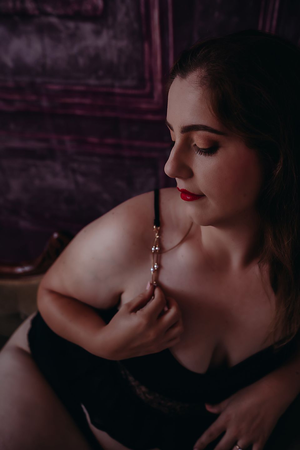 A moody boudoir photo in purple tones shows a woman in black lingerie with red lipstick in an intimate pose.