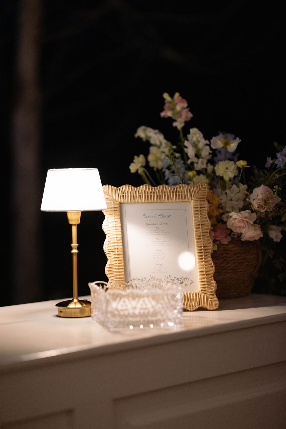 Elegant table decor with illuminated lamp, ornate picture frame, and delicate floral arrangement in soft evening light.
