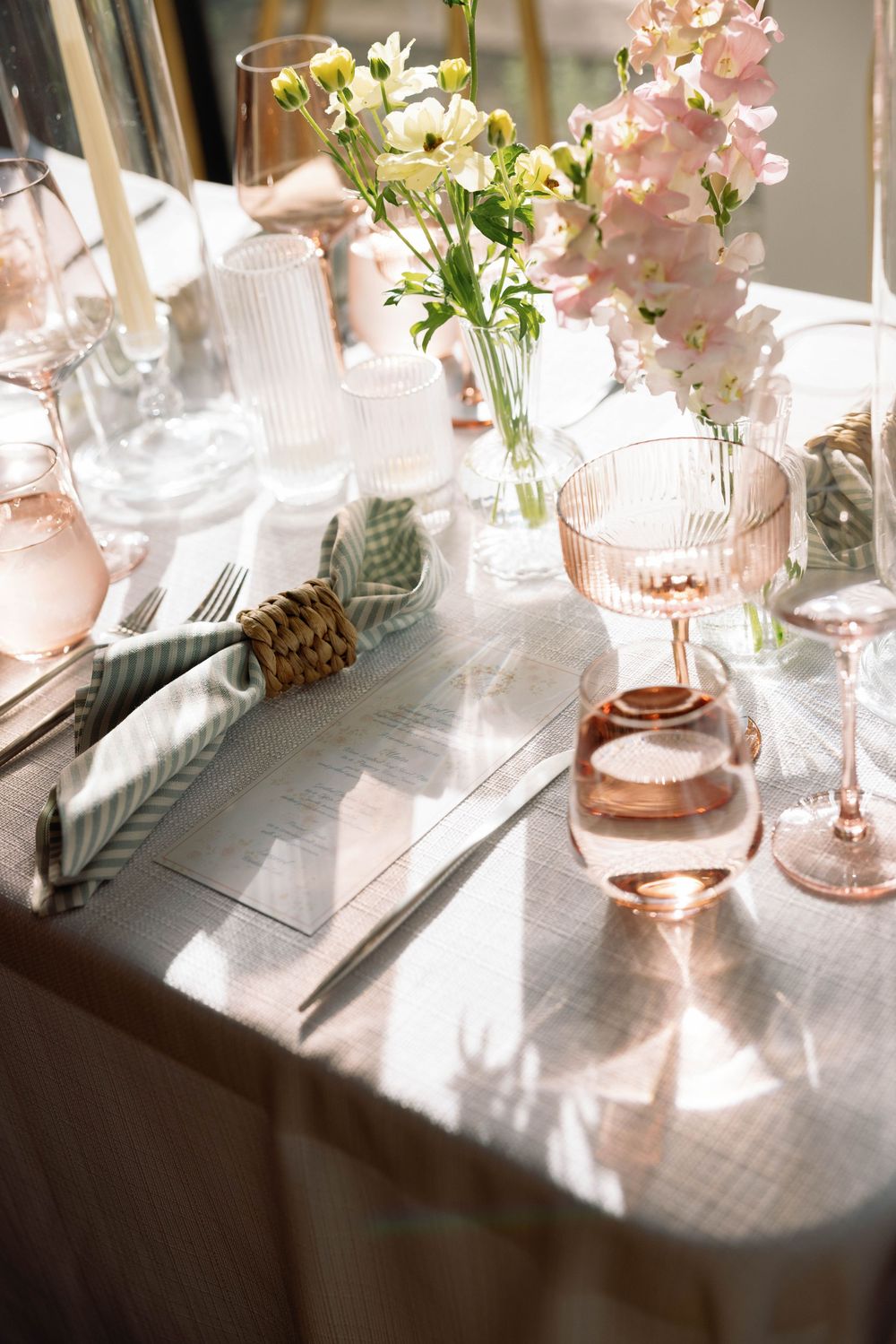 Elegant table setting with pink and white flowers in vase, rose gold glassware, and soft natural lighting.