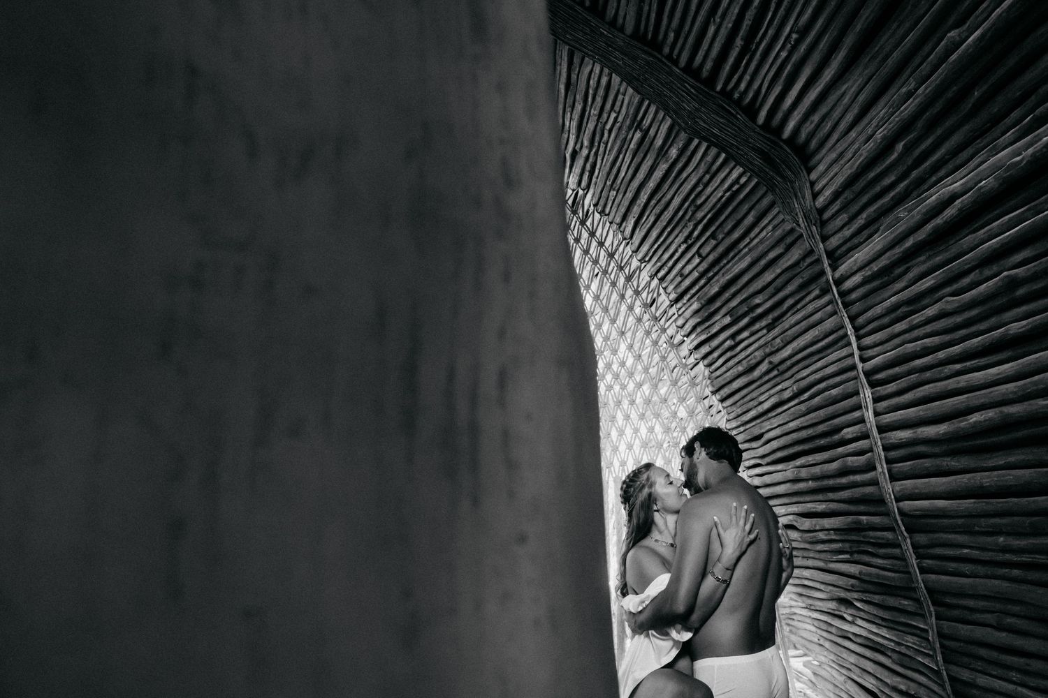 A black and white artistic photo shows an intimate couple embracing against a curved architectural feature.