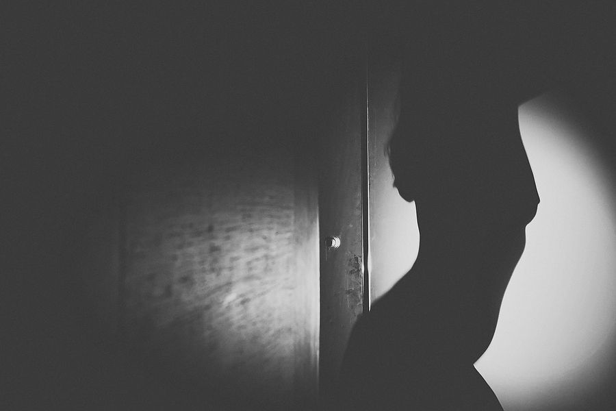 Dramatic black and white silhouette figure standing in doorway with light beam.