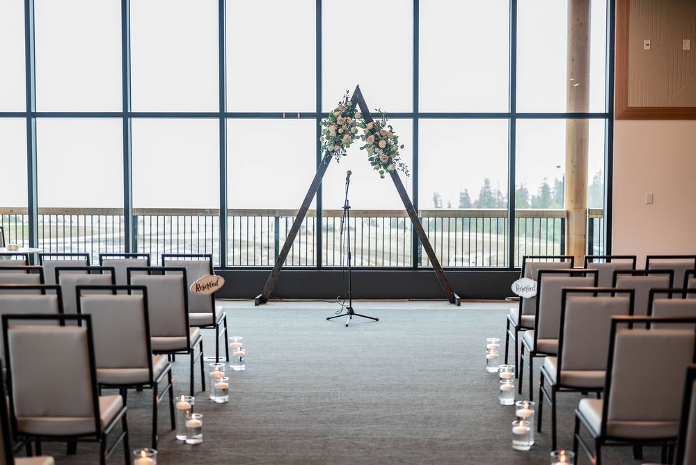 Empty chairs arranged in rows face large windows with panoramic views in a modern conference space.