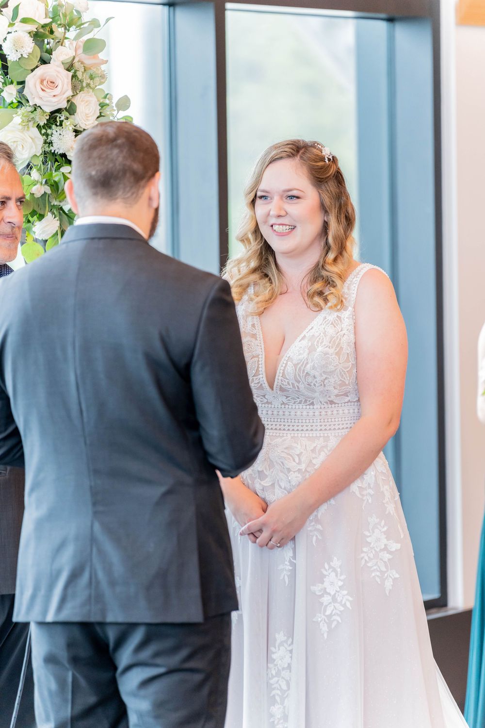 A tender wedding moment as a couple in white and gray exchange vows in front of floral decorations.